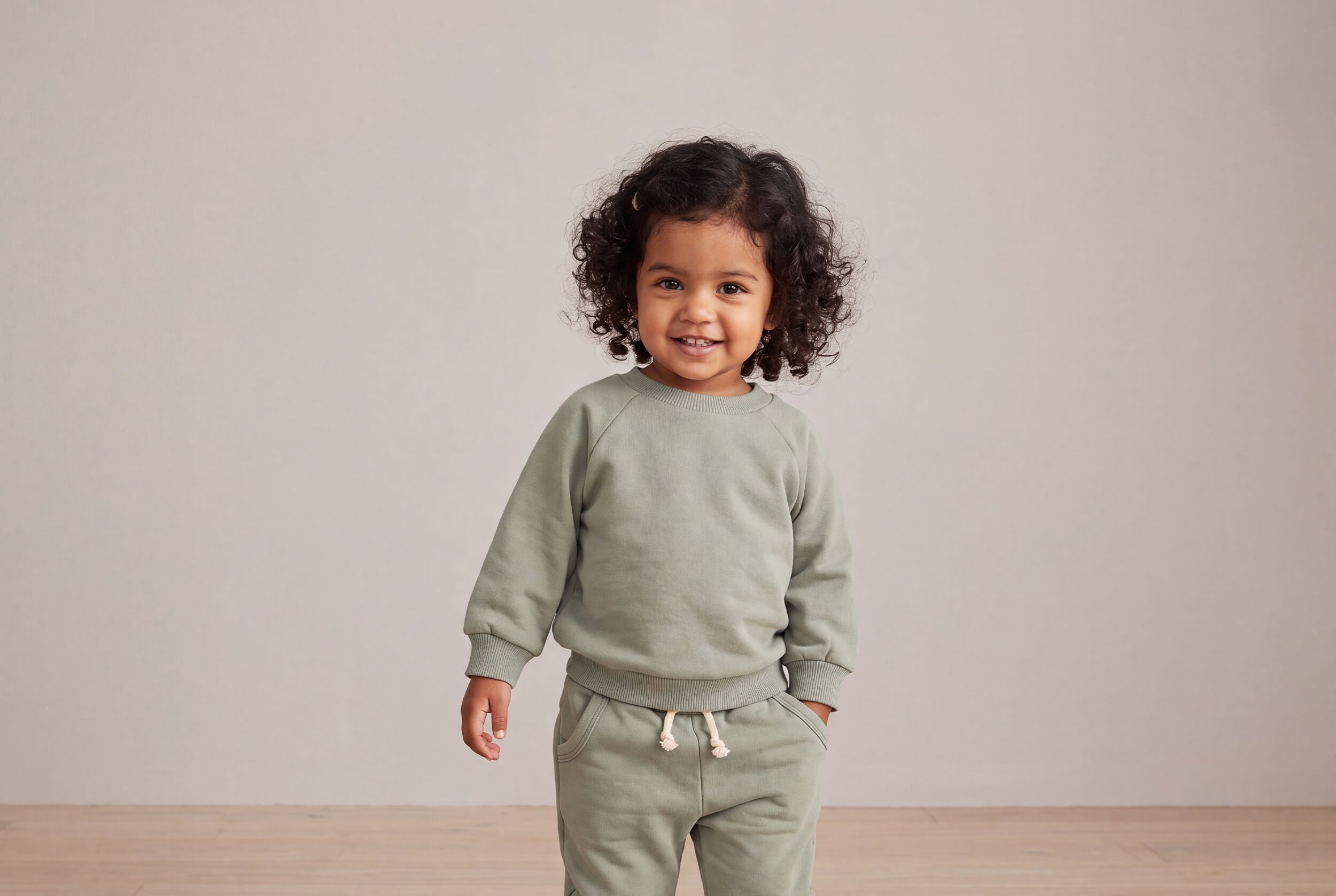 Child wearing a olive outfit sitting on a white background