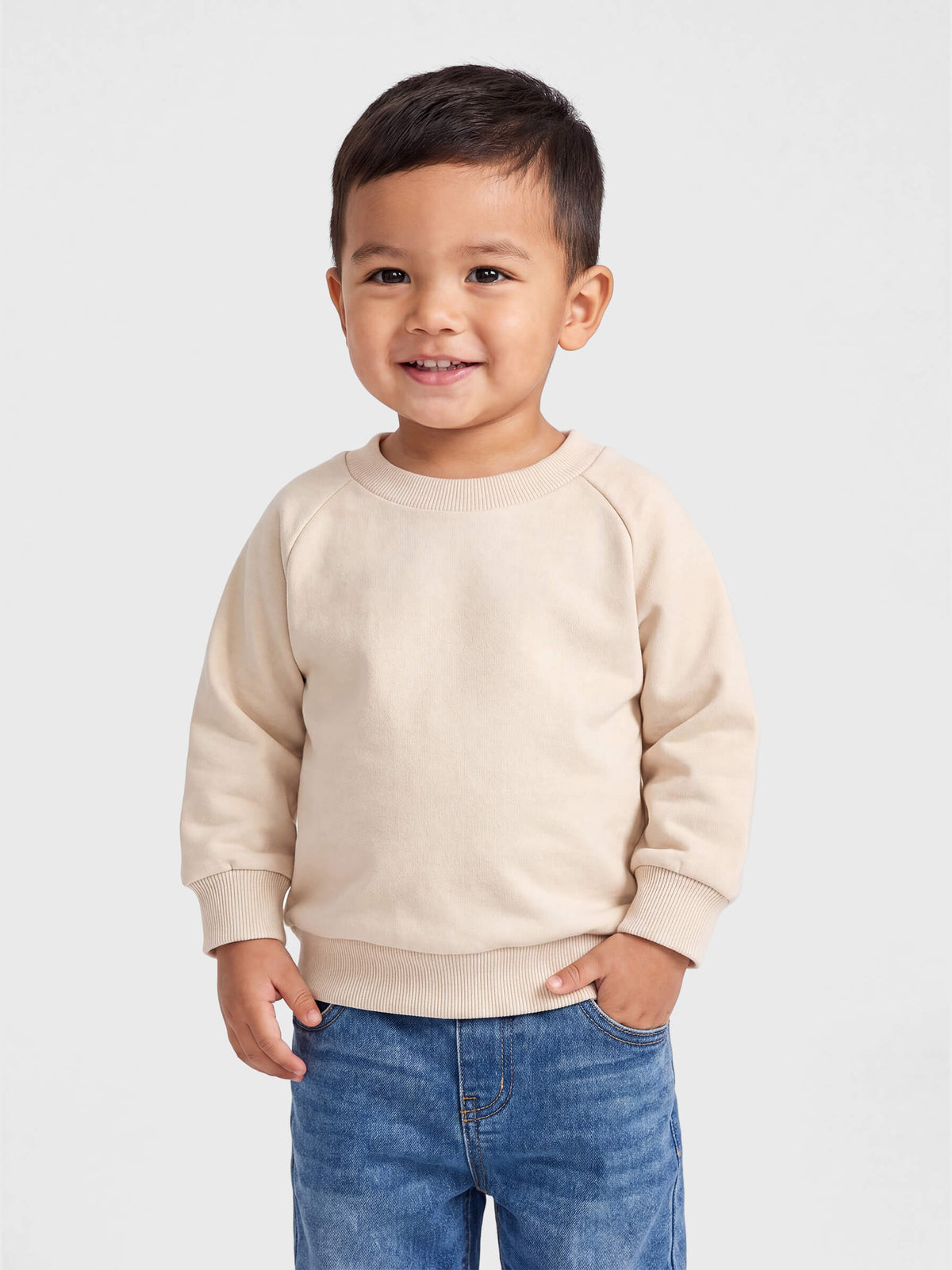 Child wearing a beige sweater and blue jeans on a light gray background